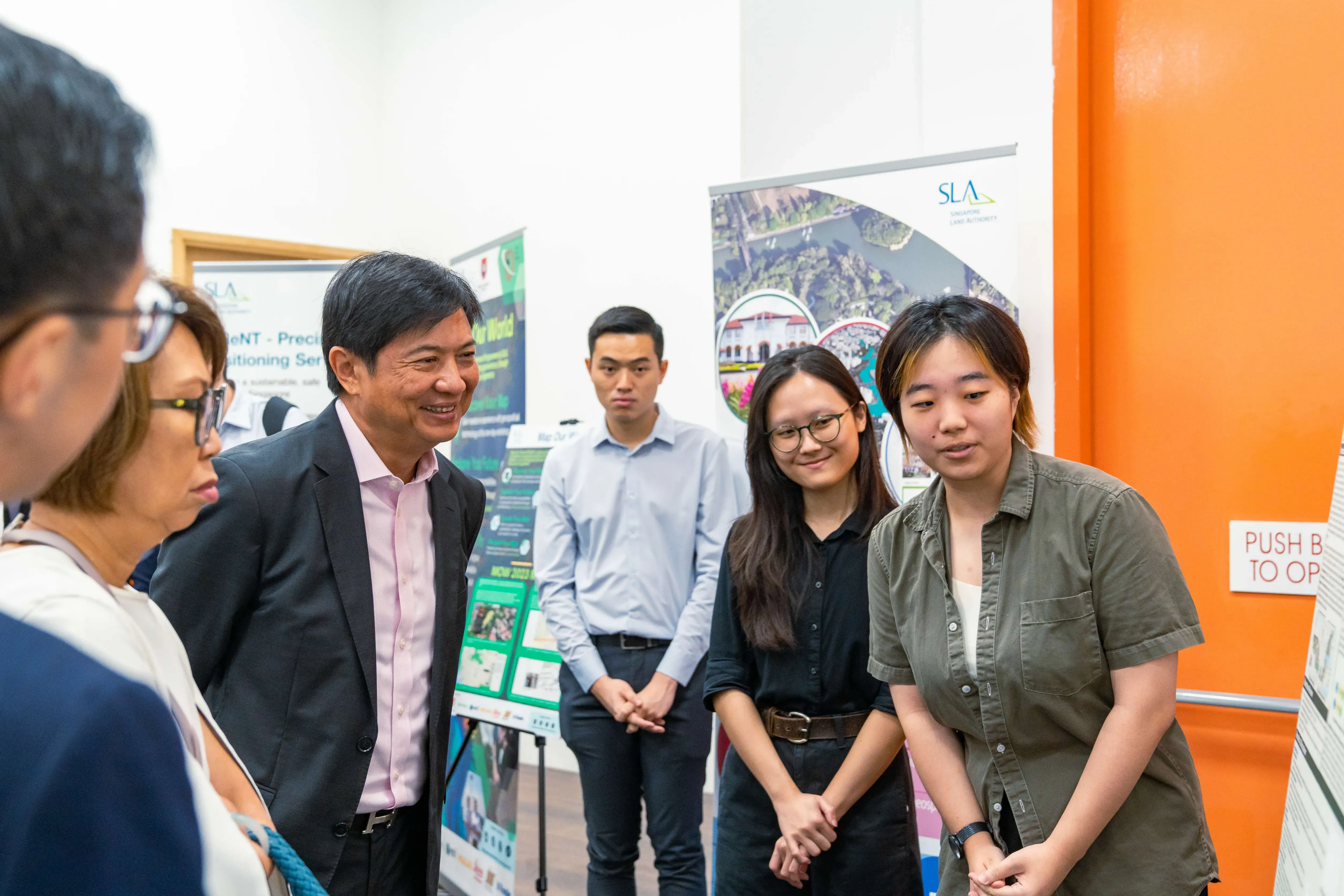 Five people stand in a room with SLA banner displays, smiling and conversing near an orange wall.